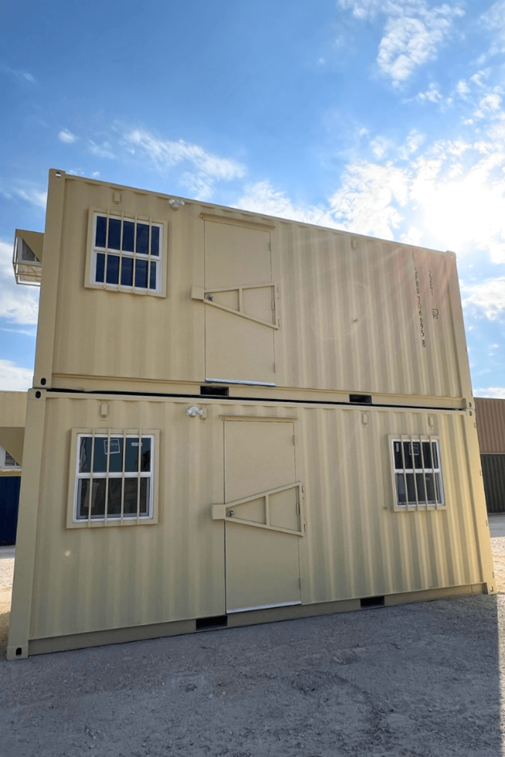 Two stacked yellow shipping containers with doors and barred windows under a blue sky.
